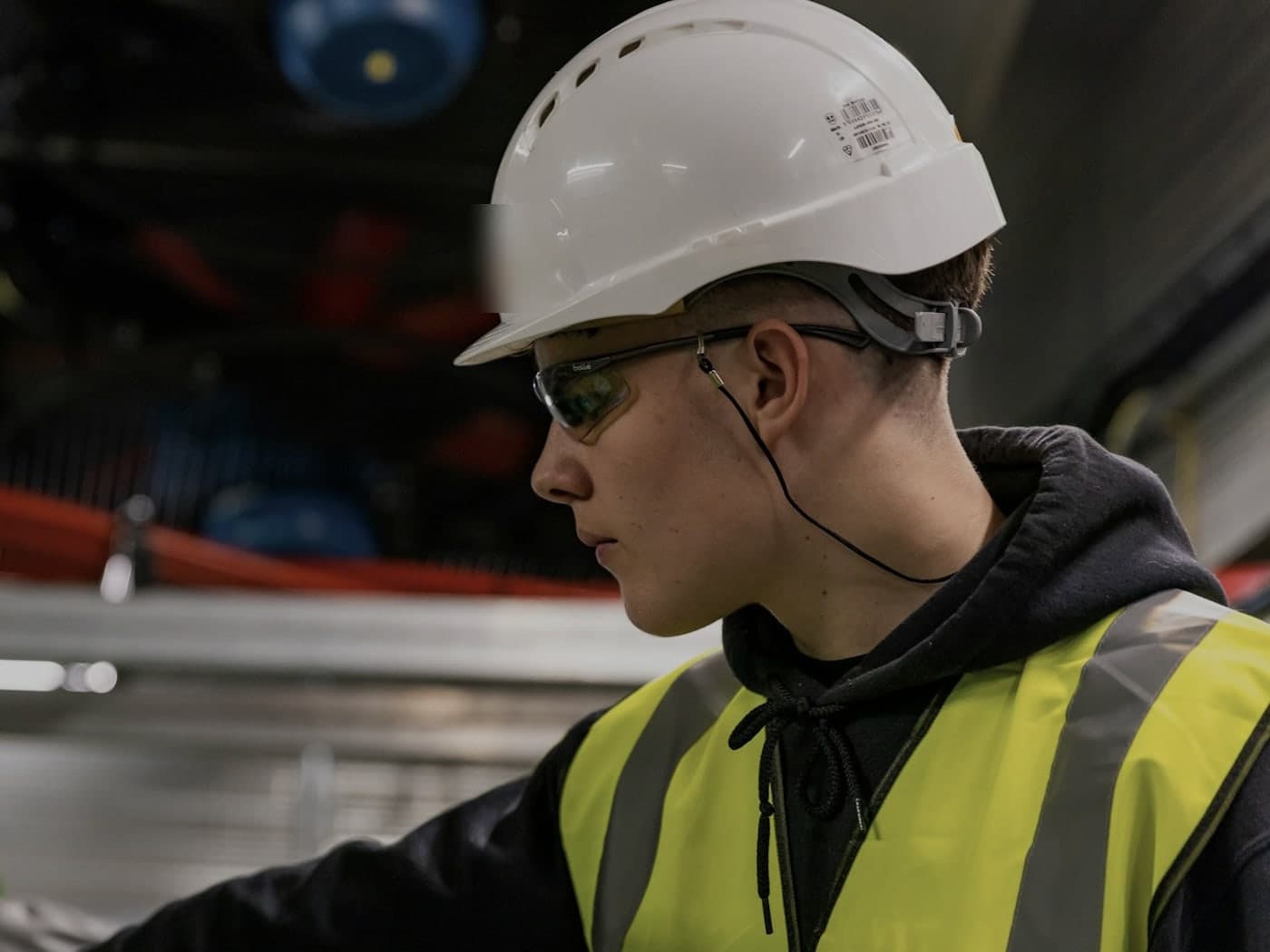 A worker in a hard hat, safety glasses and high-visibility vest, focused on the task in front of them.