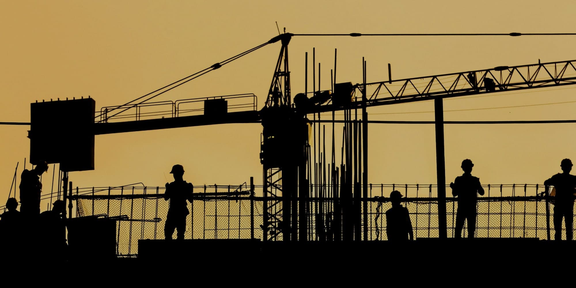 A construction crew silhouetted against a dusk sky, each worker standing at a different point on the site.